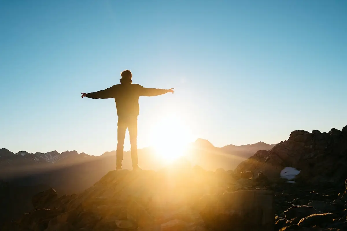 person standing with arms open towards the sunrise