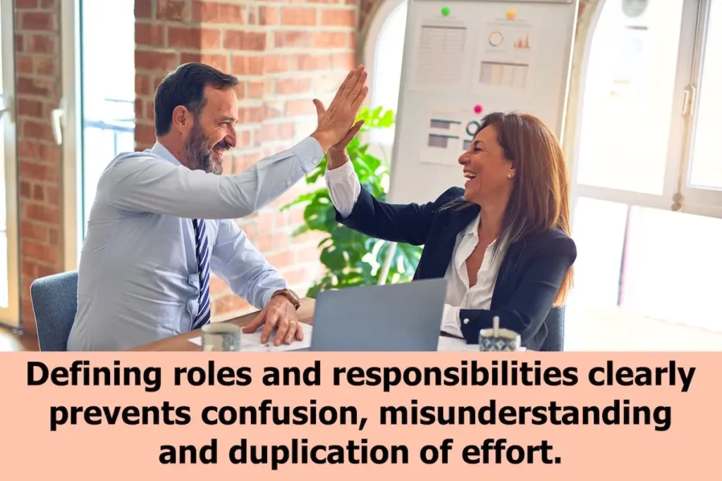 Image of 2 working executives giving each other a high-five with the text overlay: Defining roles and responsibilities clearly prevents confusion, misunderstanding and duplication of effort.