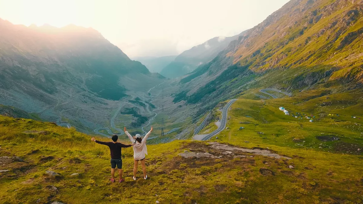 Image of a couple with their hands raised on top of a scenic hill