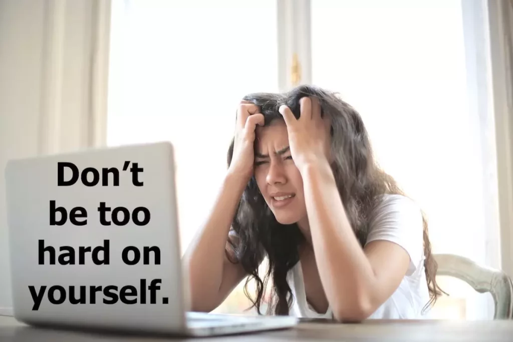 Image of a young woman sitting in front of her laptop looking distraught with the text overlay: Don't be too hard on yourself.
