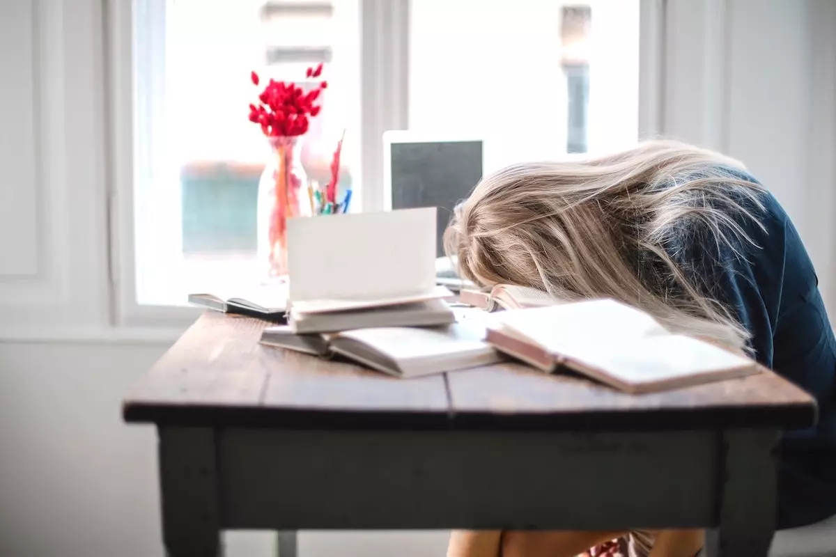 Image of a woman looking exhausted, resting her head on her work desk.